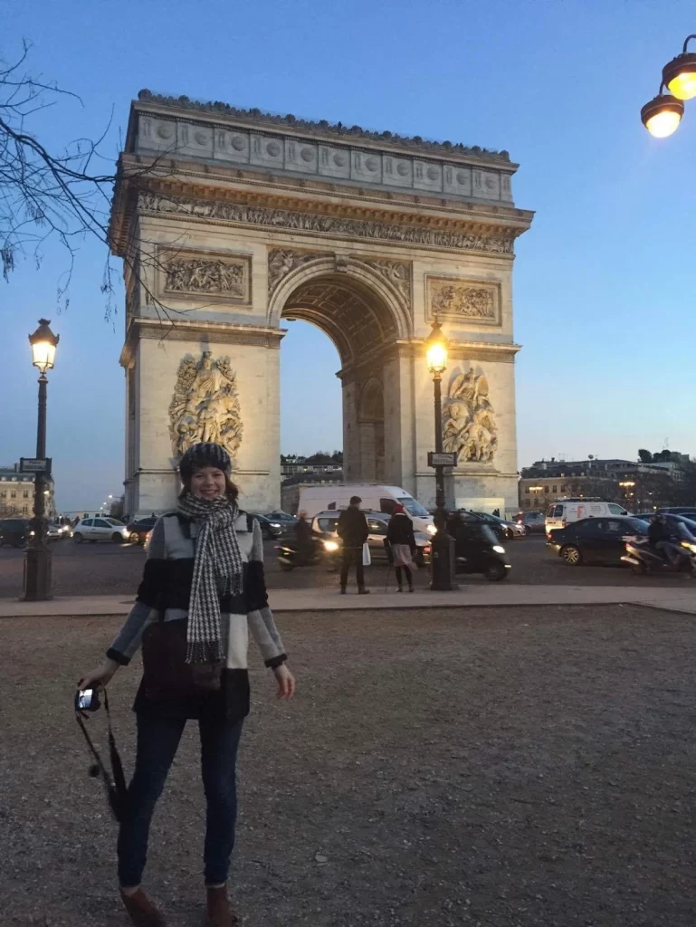 Woman standing in front of the Arc de Triomphe at dusk