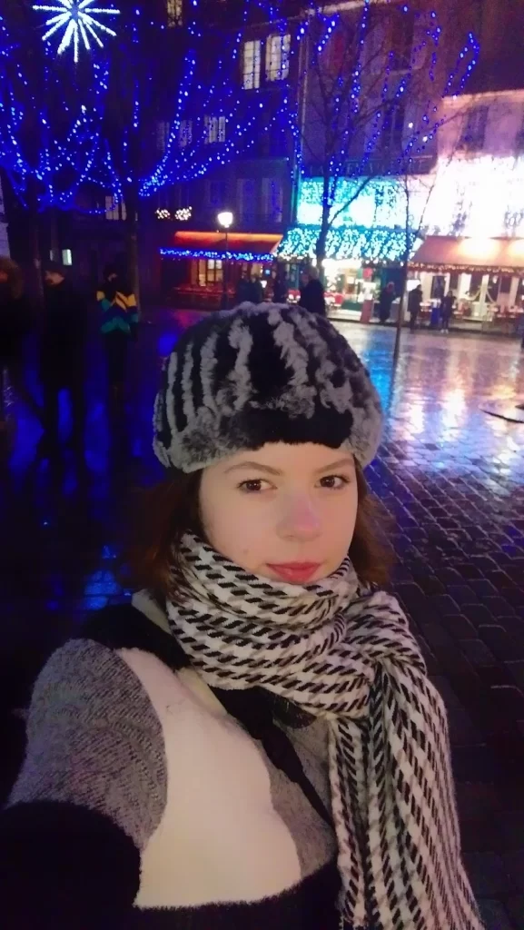 Woman on a rainy, dark street at night with Christmas lights behind her