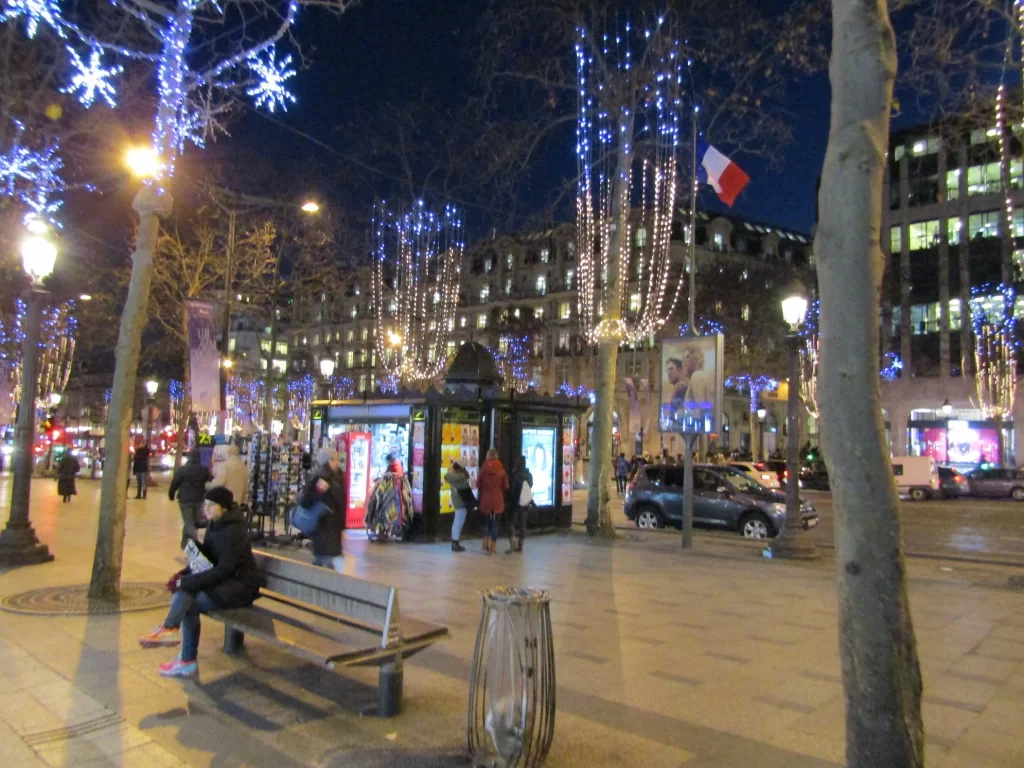 Street in Paris at night with cars, pedestrians, and Christmas lights